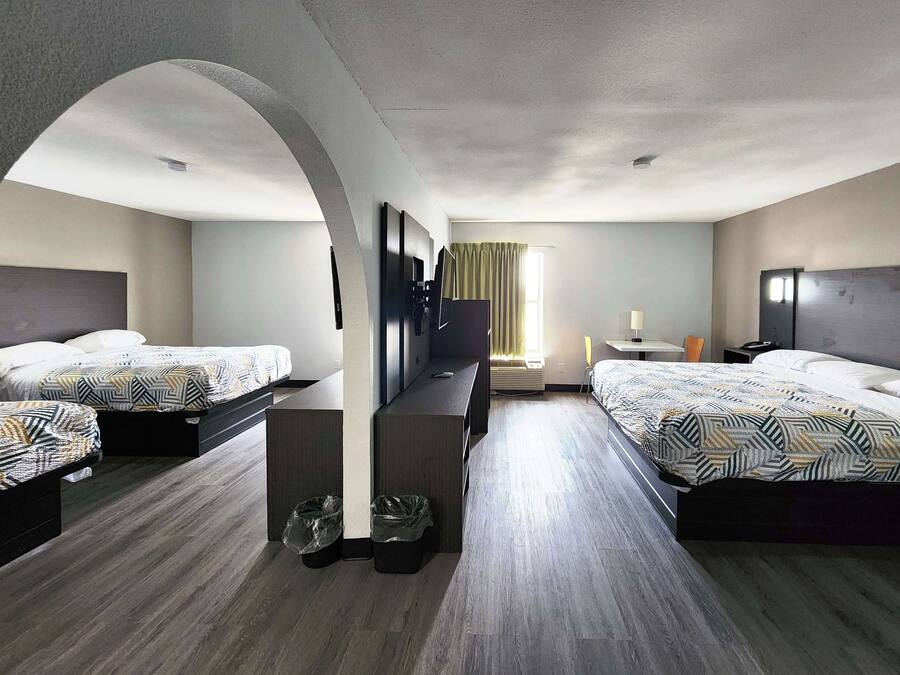 A hotel room with two beds, a TV, a desk, and a window with curtains.