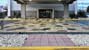 A hotel entrance with a geometric patterned floor, a bench, and a clear sky view.