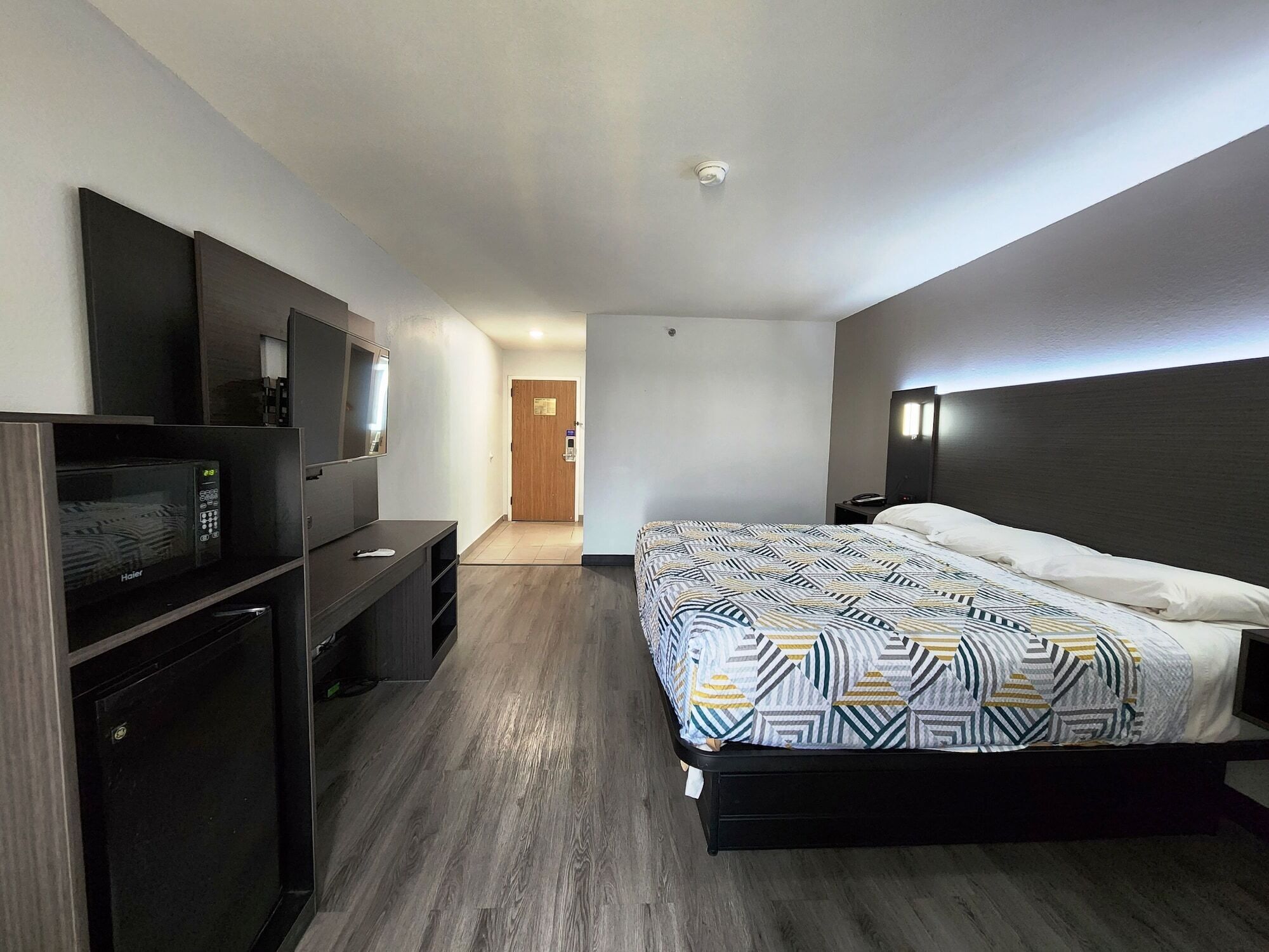 A modern hotel room with a bed, a desk, a vanity, and a television.