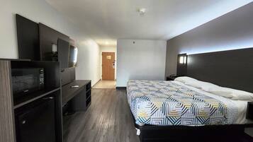 A modern hotel room with a bed, a desk, a vanity, and a television.