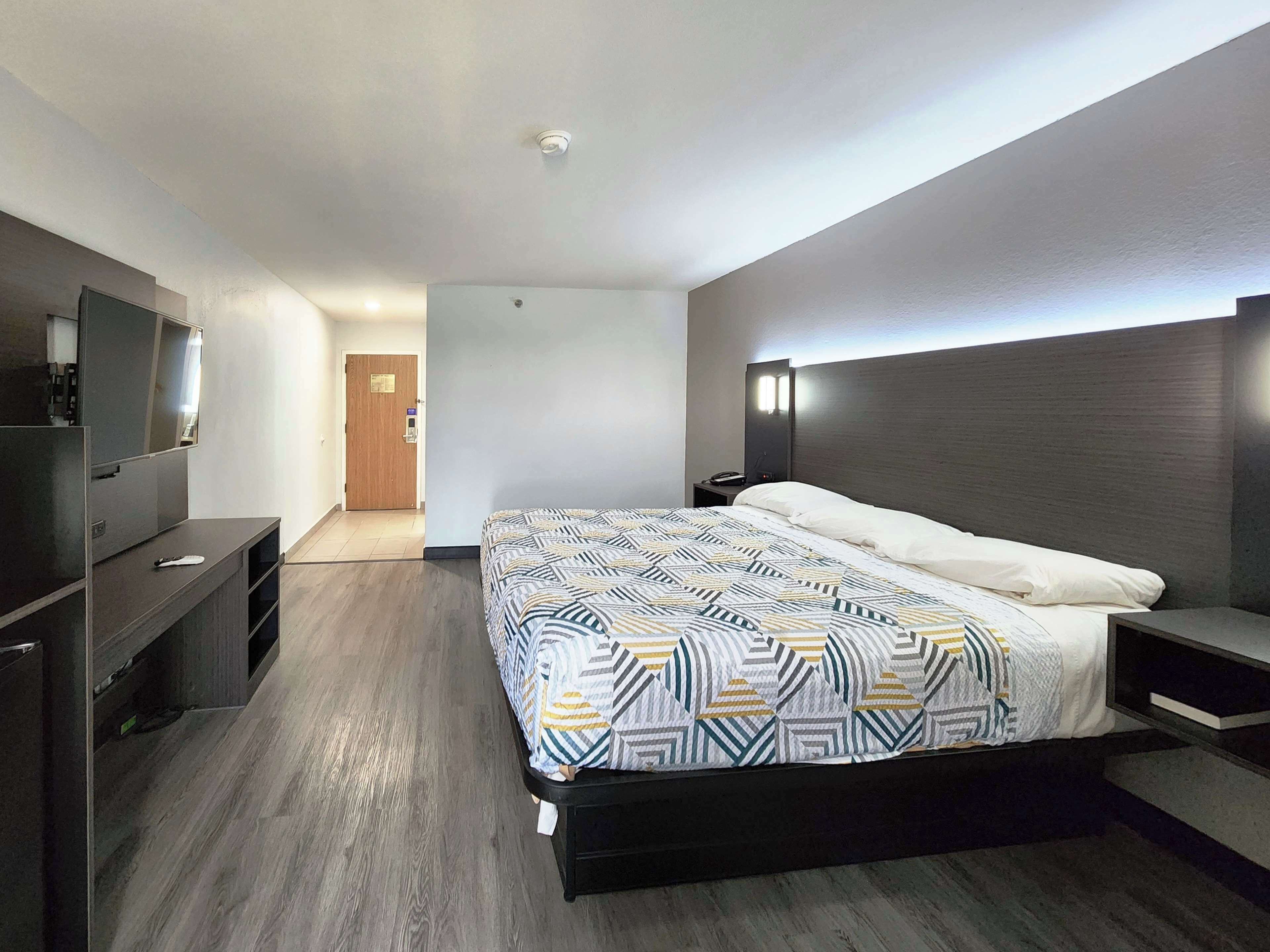 Una habitación de hotel moderna con una cama grande, un televisor de pantalla plana, una mesita de noche y un buró.