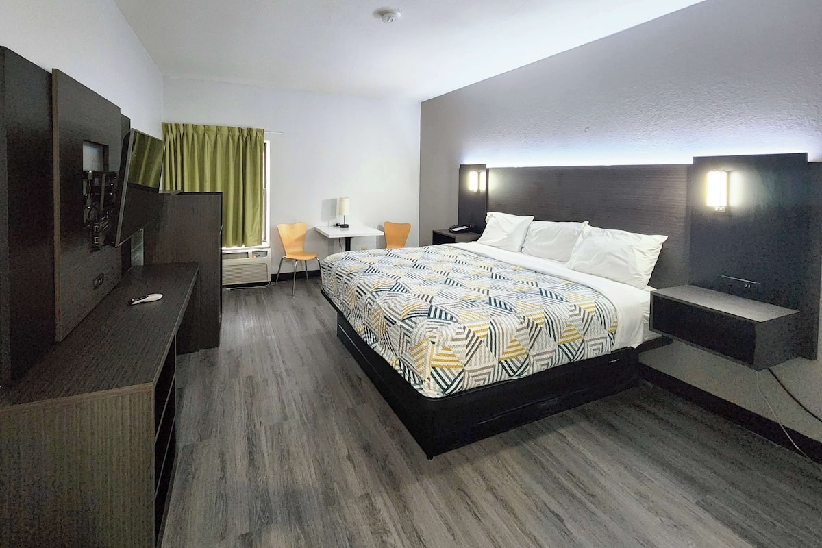 A hotel room with a large bed, a desk, a chair, and a TV.