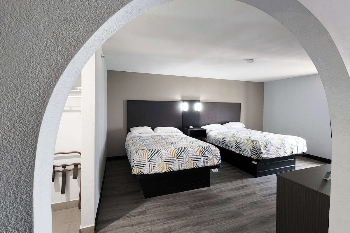 A modern hotel room with two beds, a nightstand, and a desk.