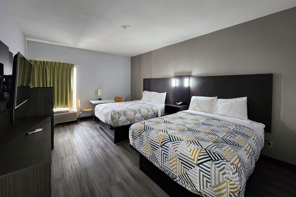 A hotel room with two beds, a desk, a chair, a TV, and a window with curtains.