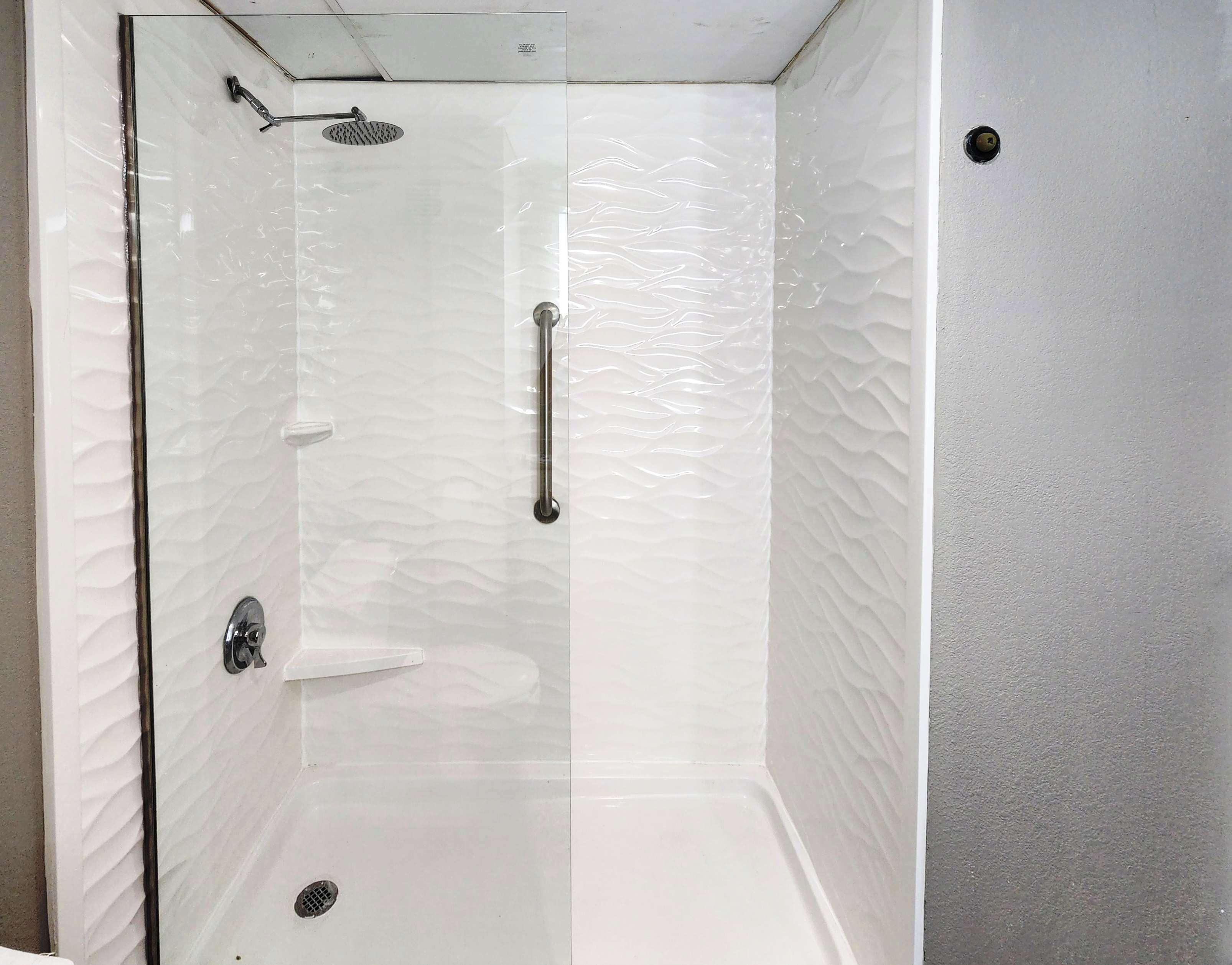 A glass-enclosed shower with a textured wall, a handheld showerhead, and a control lever.