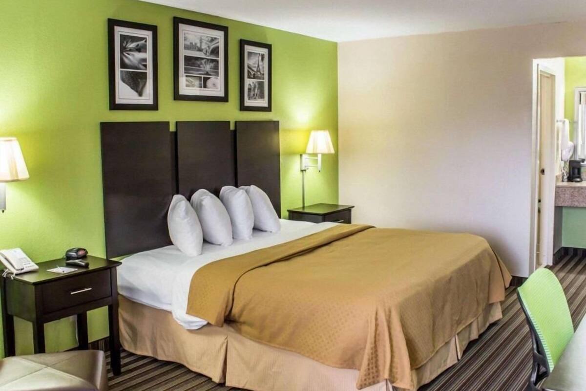 Ein Hotelzimmer mit einem Bett, zwei Nachttischen, einem Sessel und drei gerahmten Bildern an der Wand.