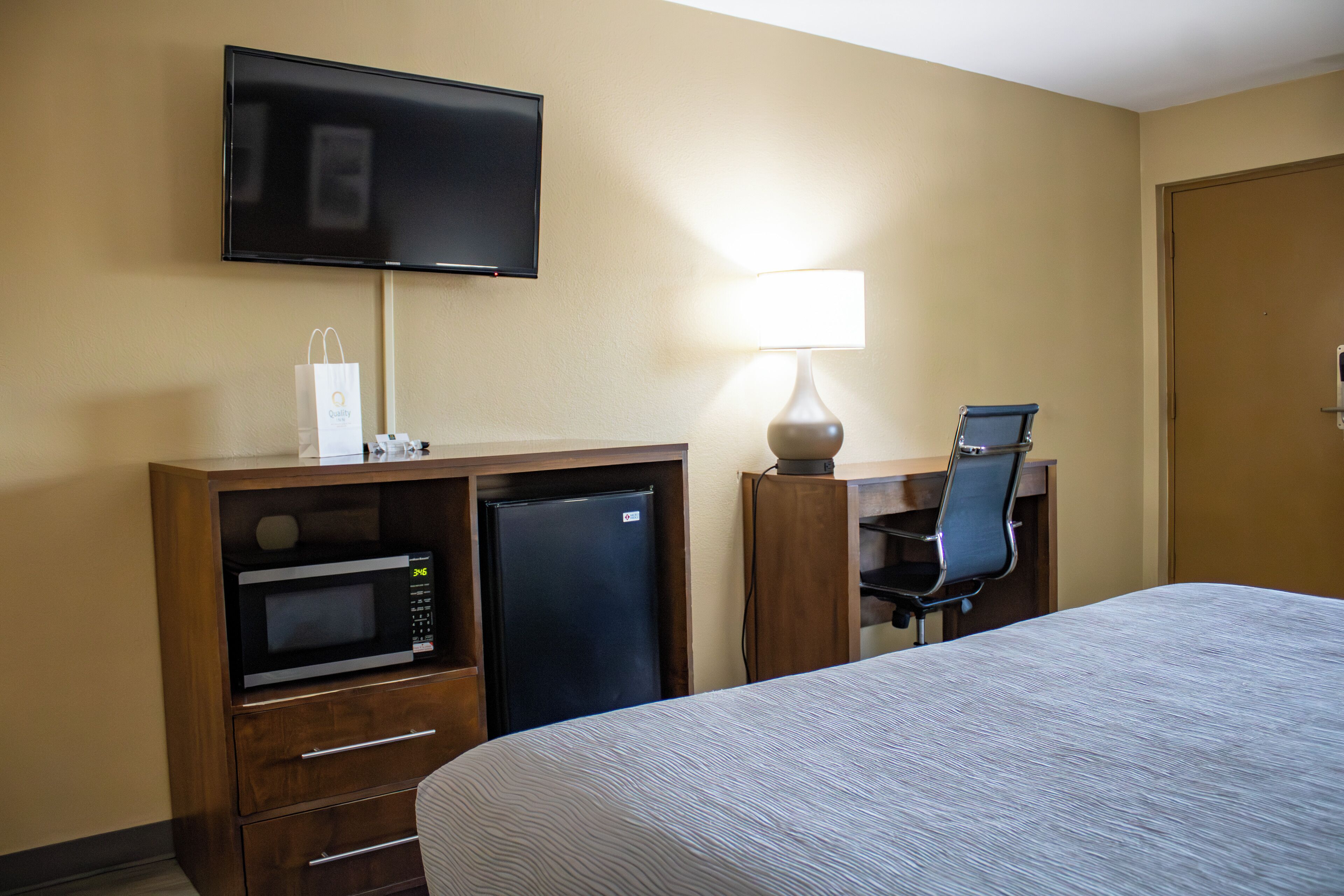 A hotel room with a bed, a desk with a chair, a television, a microwave, and a refrigerator.