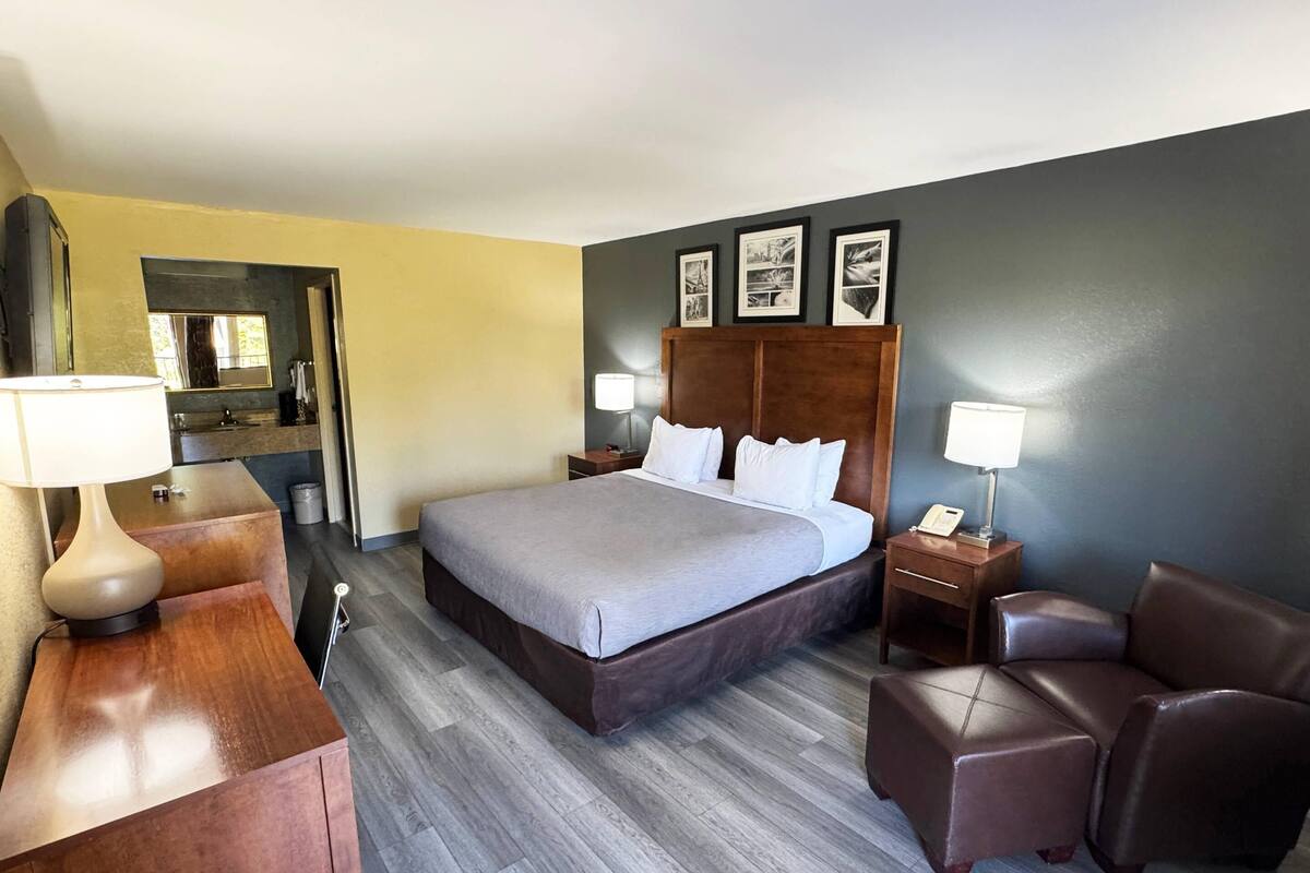 Ein Hotelzimmer mit einem Bett, Nachttischen, einem Sessel, einem Schreibtisch und einem Spiegel.