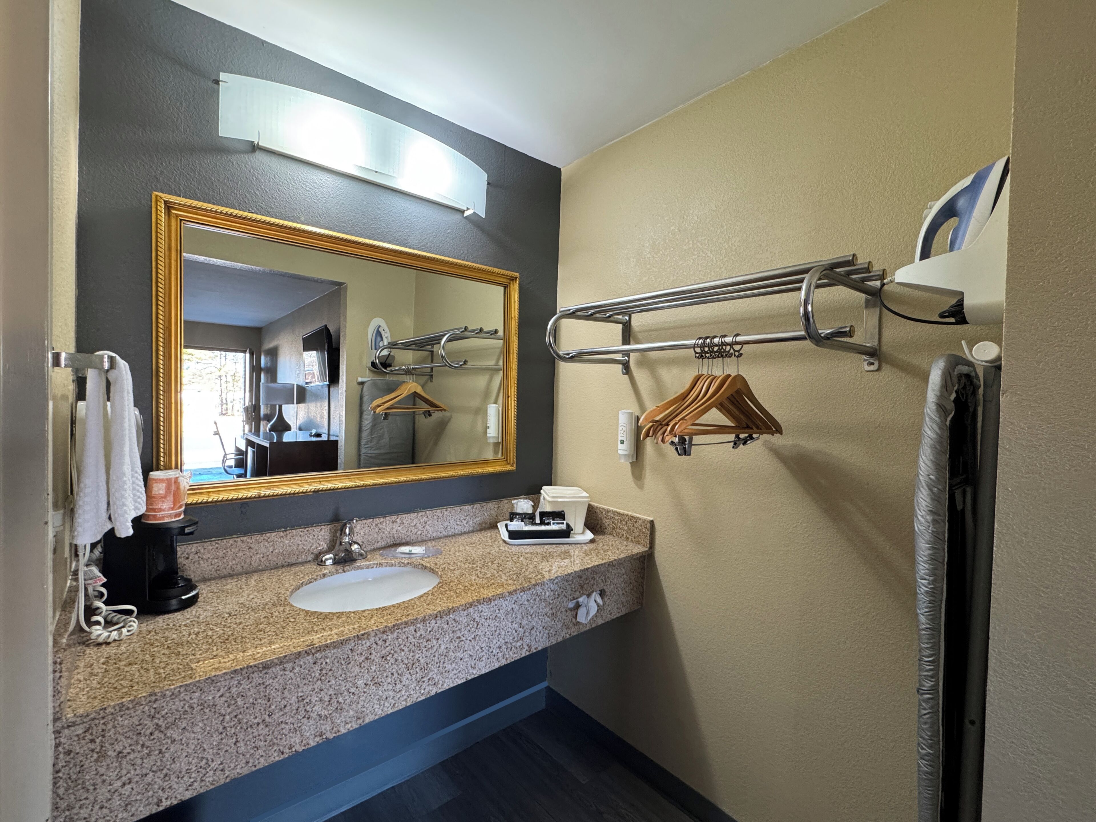 A bathroom with a sink, mirror, towel rack, and towel dispenser.
