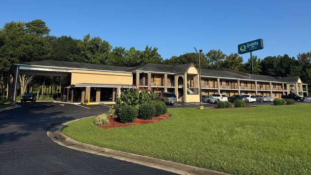 A motel with a covered entrance, multiple parking spaces, and a clear sky.