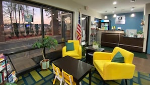 A reception area with a reception desk, yellow chairs, a table, and a potted plant.