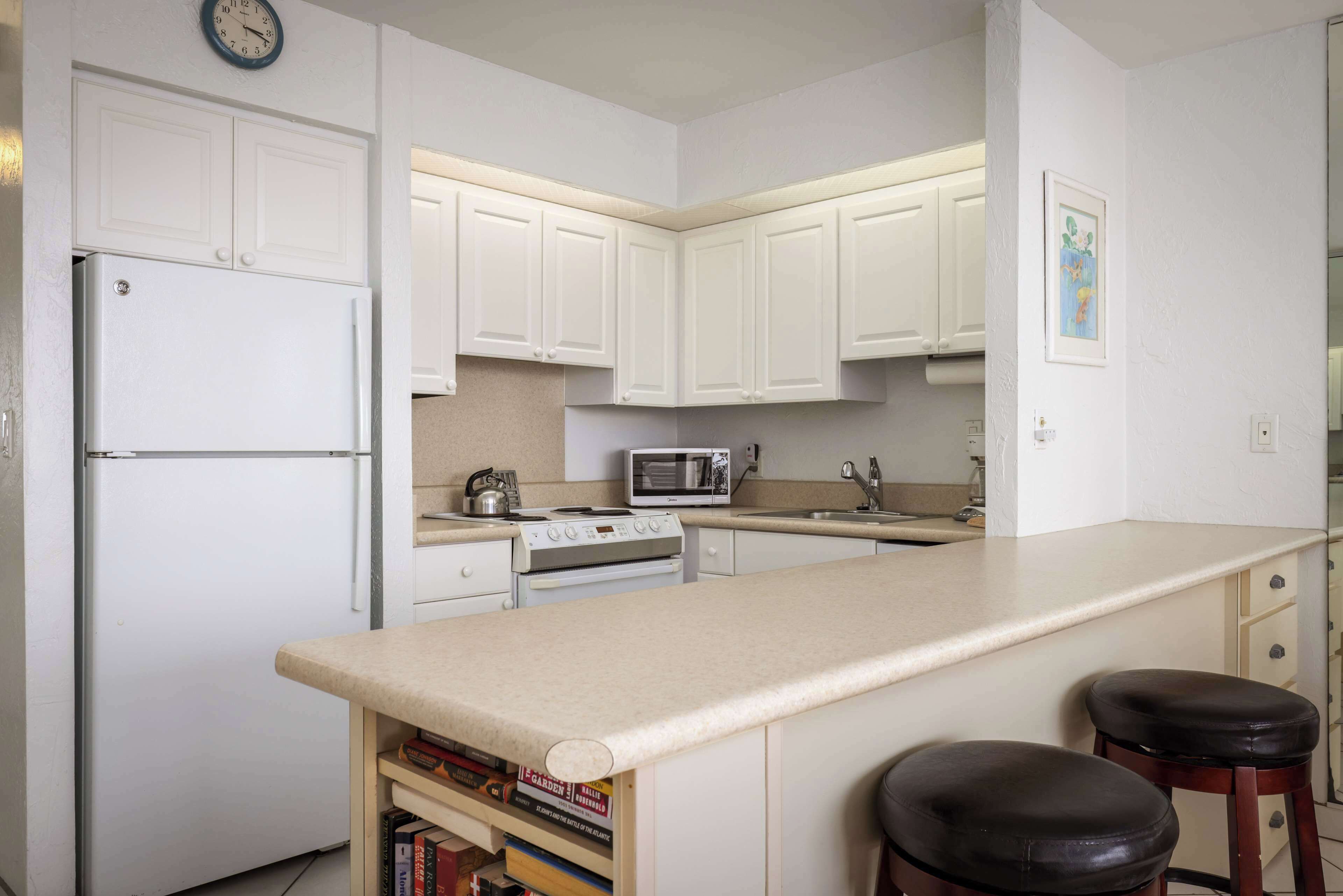 A kitchen with white cabinets, a refrigerator, a microwave, a stove, and two bar stools.