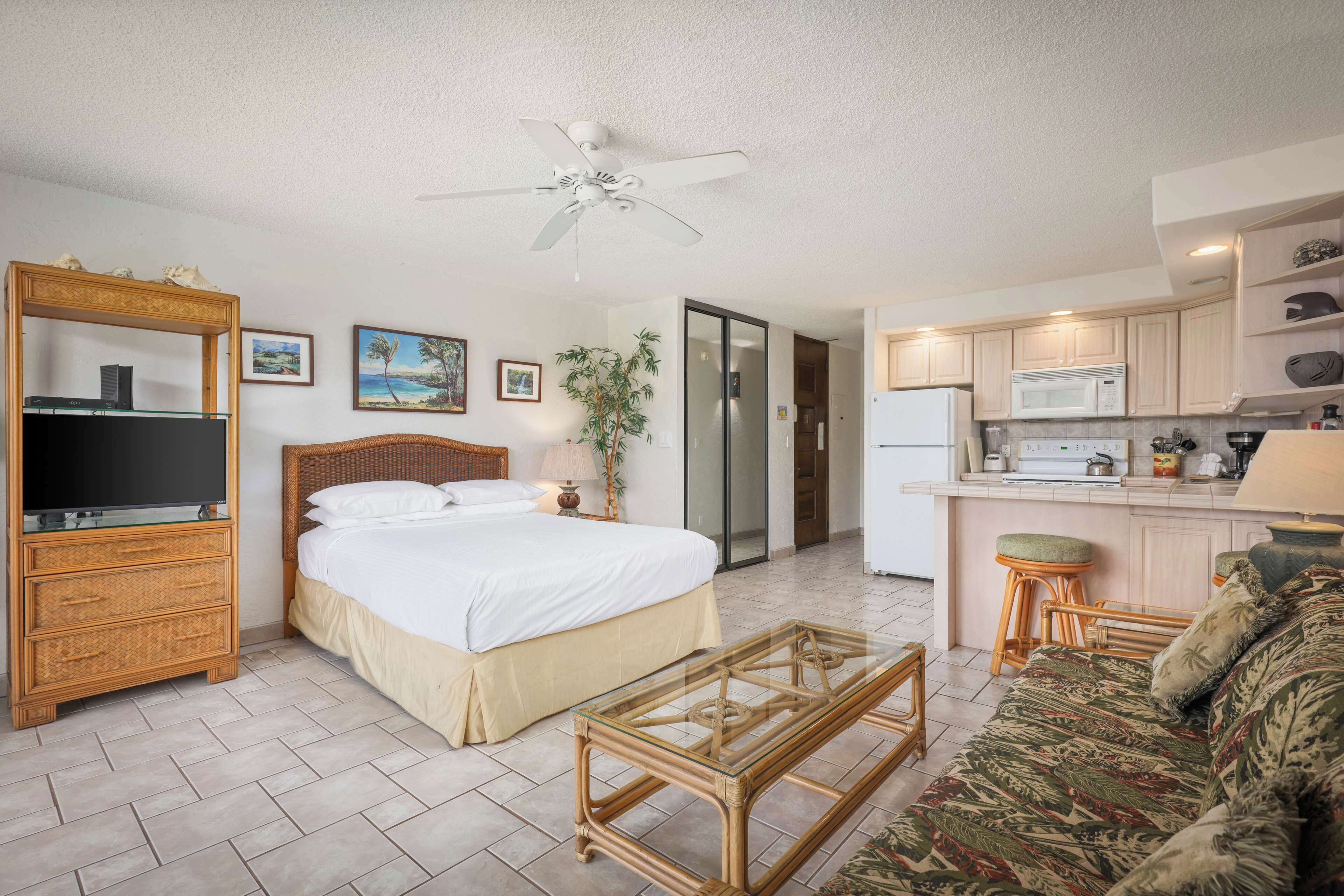 A hotel room with a bed, a television, a dining area with a microwave, and a ceiling fan.