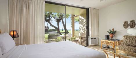 A hotel room with a large bed, a ceiling fan, a sliding glass door leading to a balcony with a view of palm trees and the ocean.
