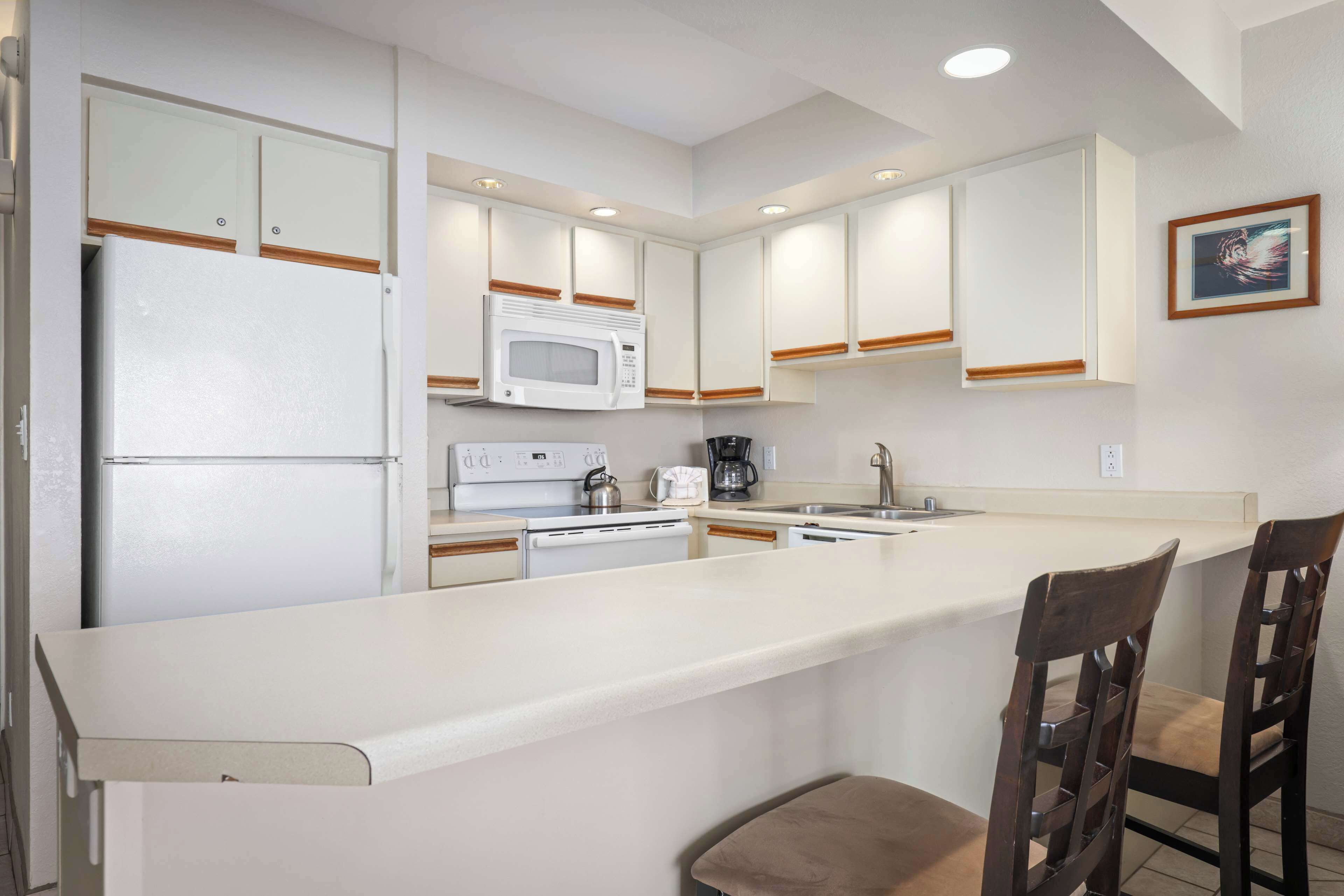 A kitchen with white cabinets, a microwave, a coffee maker, and a bar area with two wooden chairs.