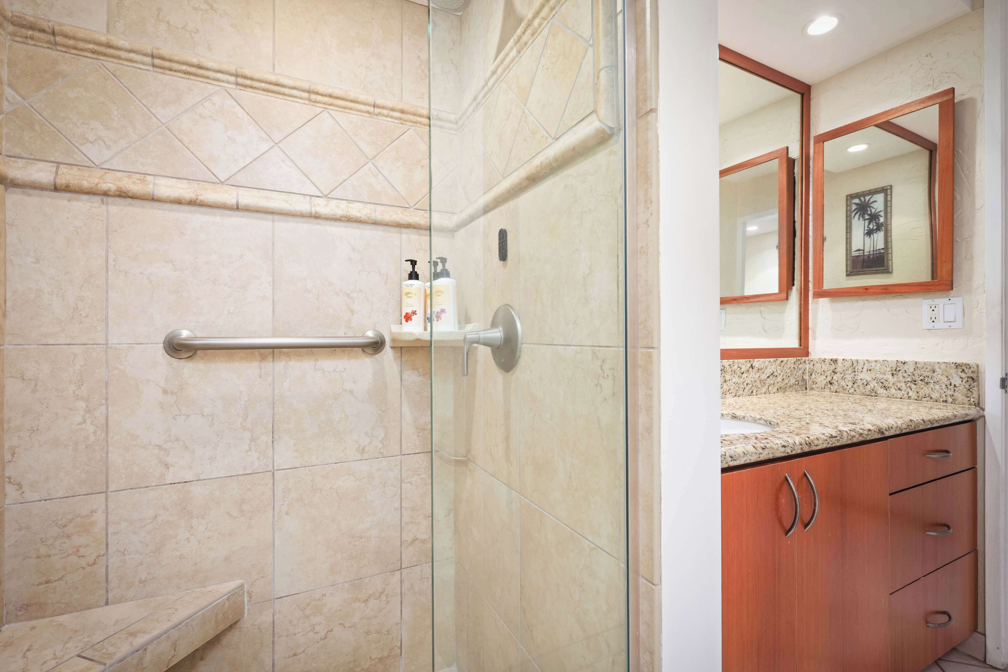 Une salle de bain avec une douche à parois de verre, une barre d’appui, des toilettes et un meuble-lavabo avec un miroir et un placard.
