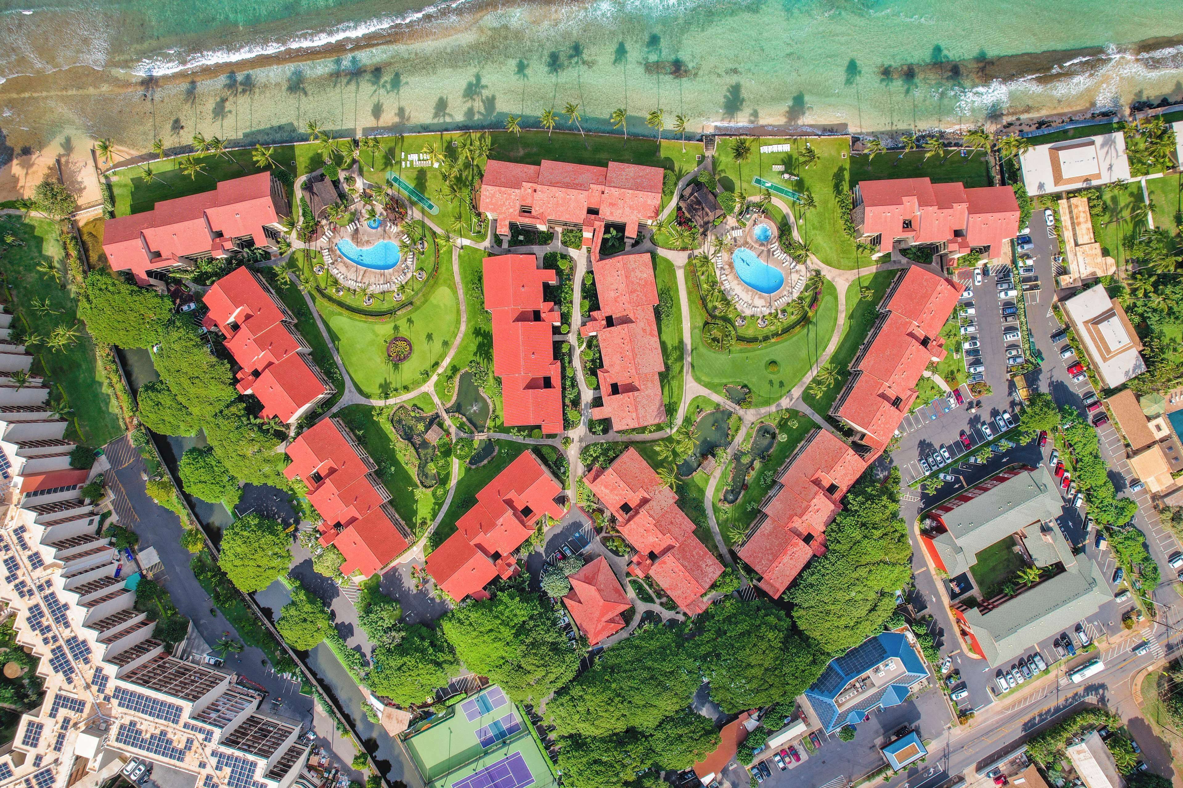 An aerial view of a resort with multiple red-roofed buildings, a swimming pool, and a beach area.