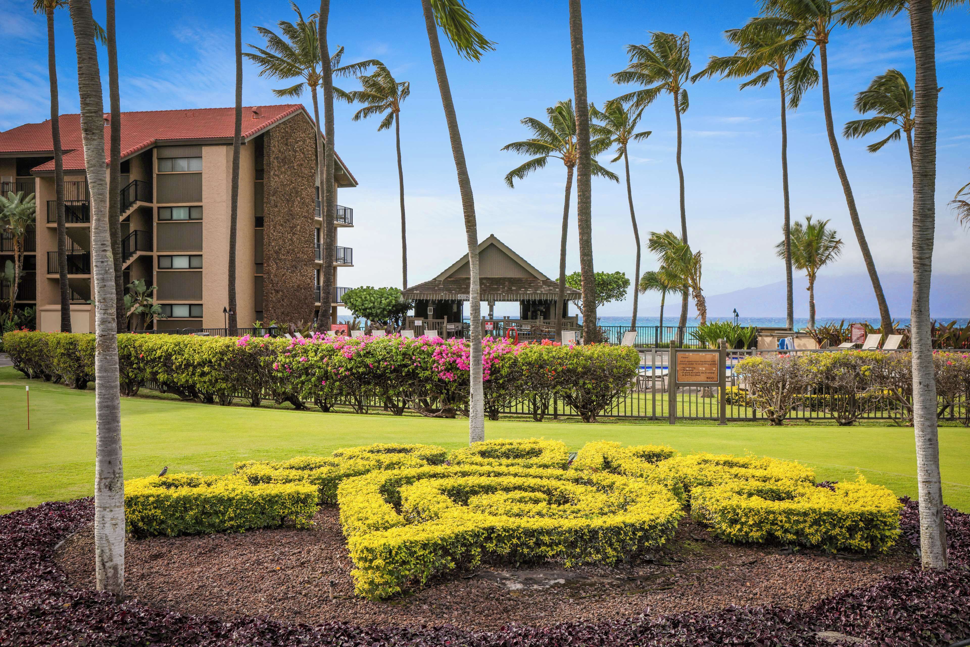 Un hotel con piscina, palmeras y un jardín ajardinado con flores amarillas.