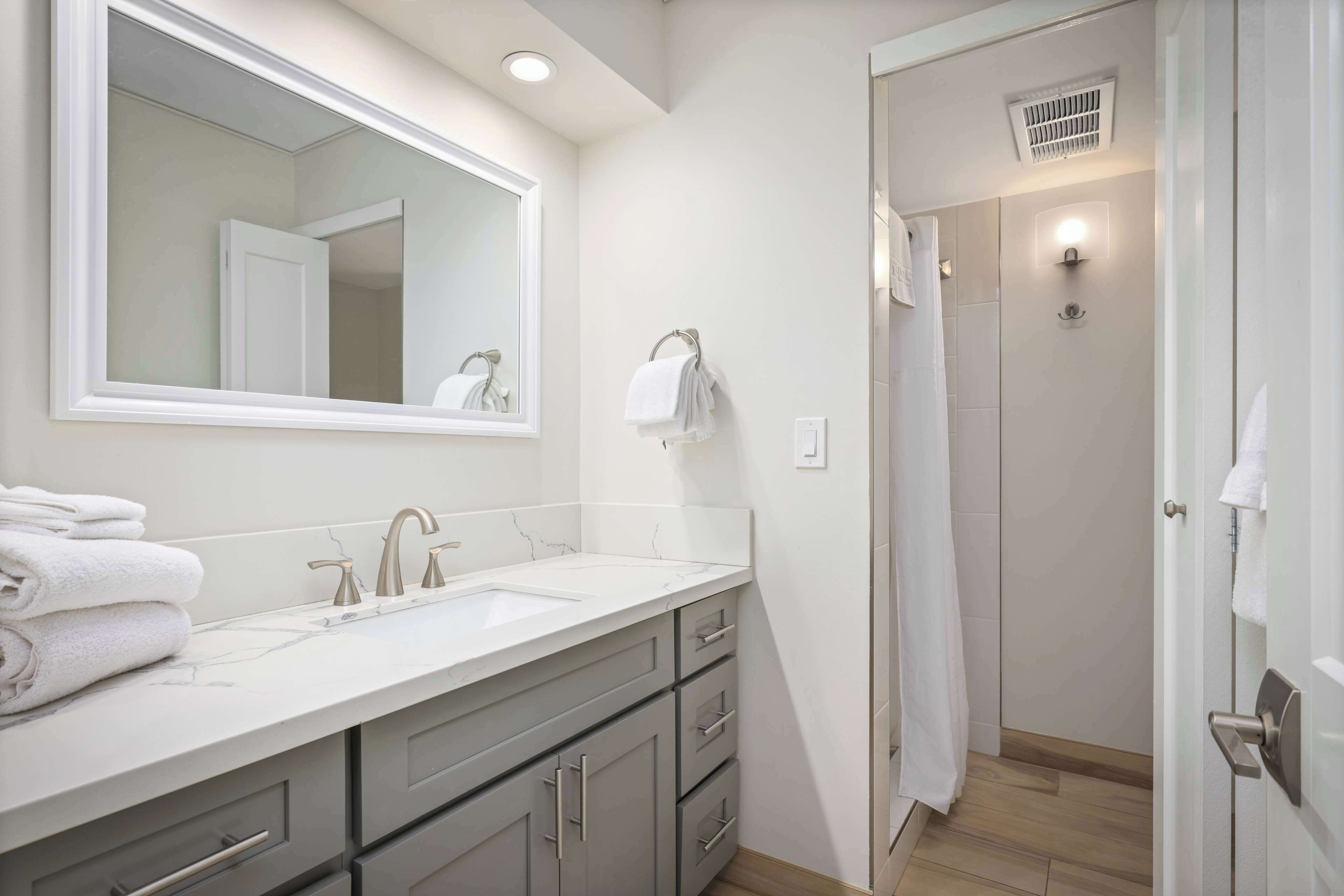 Un baño moderno con tocador blanco, un espejo grande y una zona de ducha.