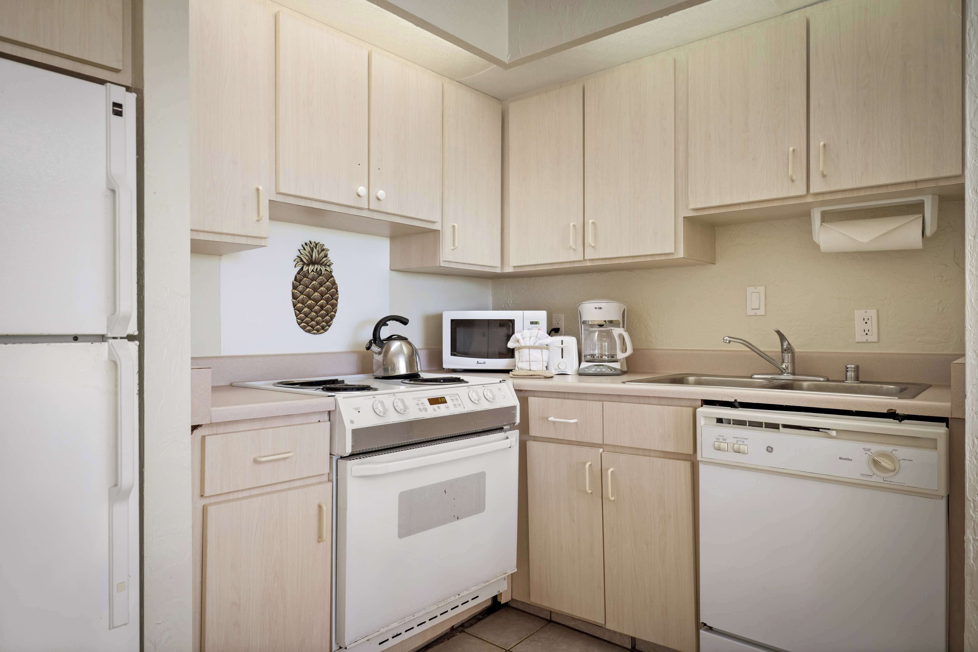 Una cocina con armarios de madera clara, un refrigerador blanco, una estufa, un microondas, una cafetera y un lavavajillas.