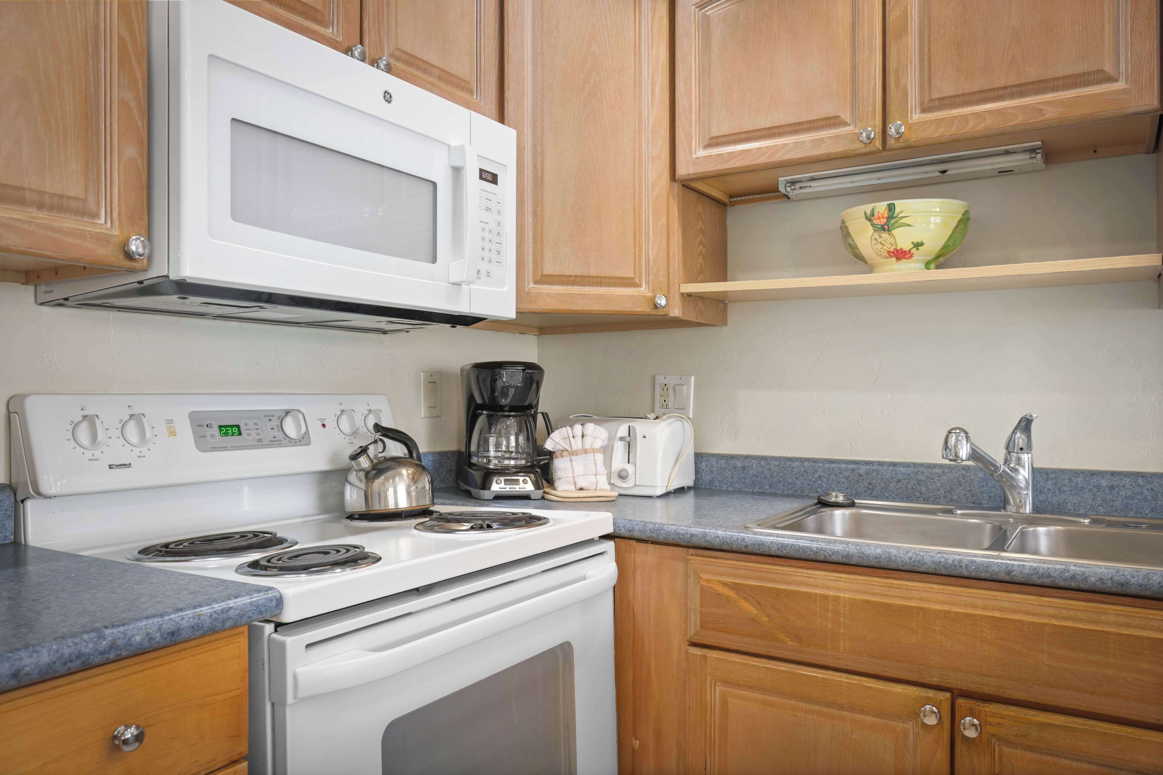 A kitchen with wooden cabinets, a white stove, a microwave, a coffee maker, a toaster, and a sink.