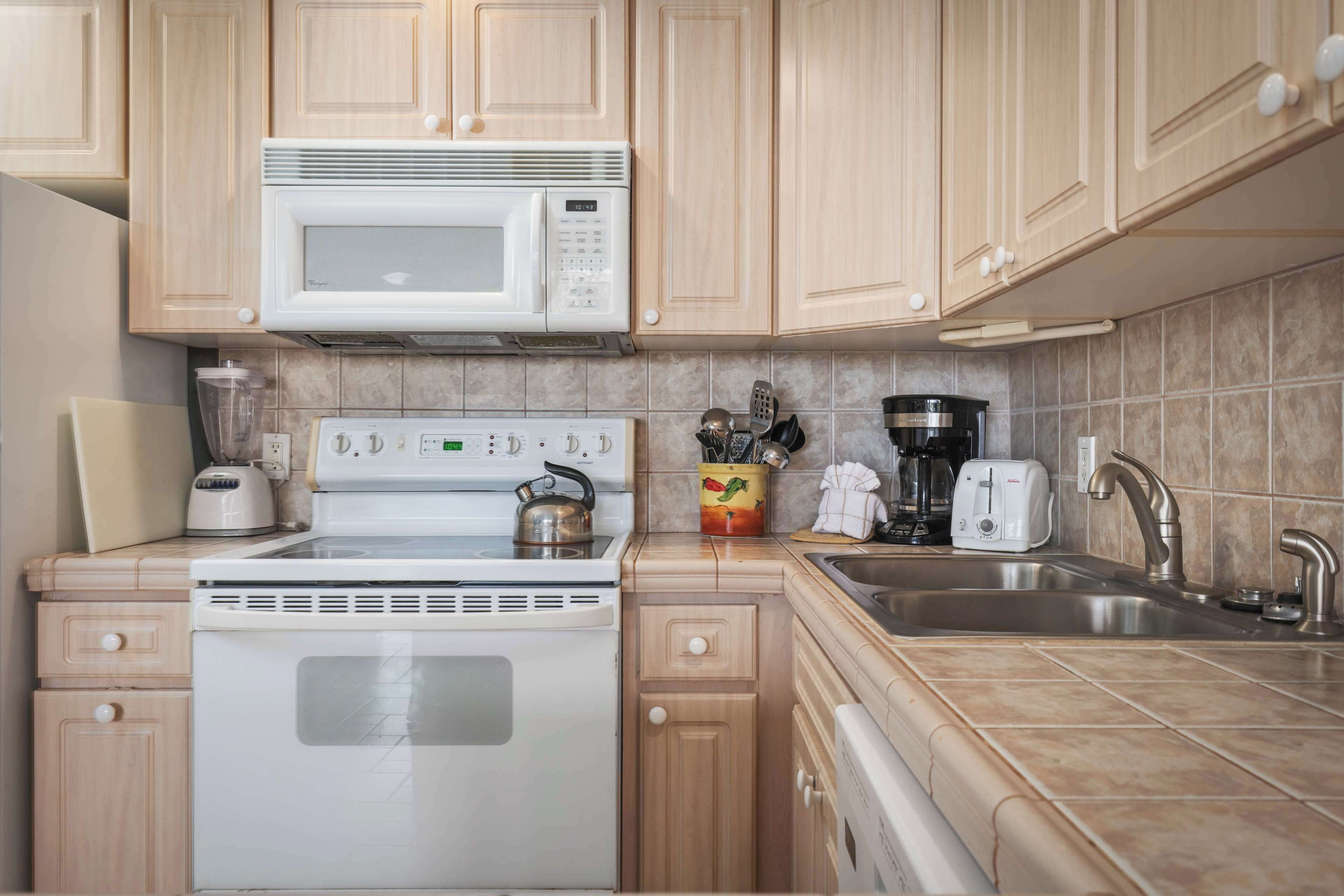 Una cocina con armarios de madera, una estufa blanca, un microondas, un tostador, una cafetera y un fregadero.