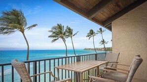 A wooden table and chairs on a balcony with a view of the ocean and palm trees.
