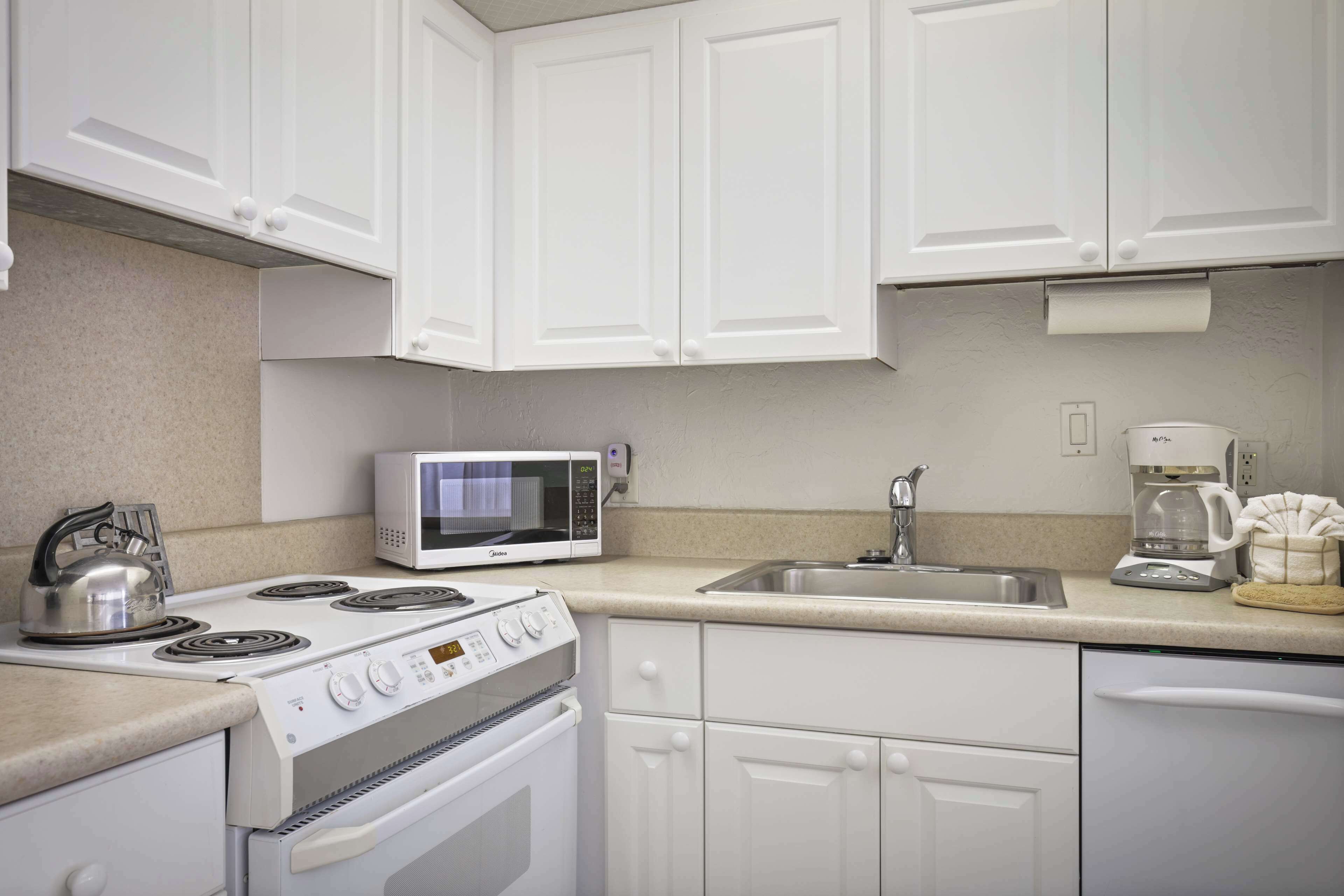 A kitchen with white cabinets, a stove, a microwave, a sink, and a coffee maker.