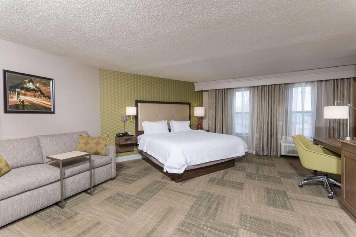 A hotel room with a bed, a sofa, a desk, and a chair.
