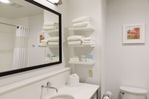 A bathroom with a white sink, mirror, and toilet. There are shelves with folded towels and toiletries.