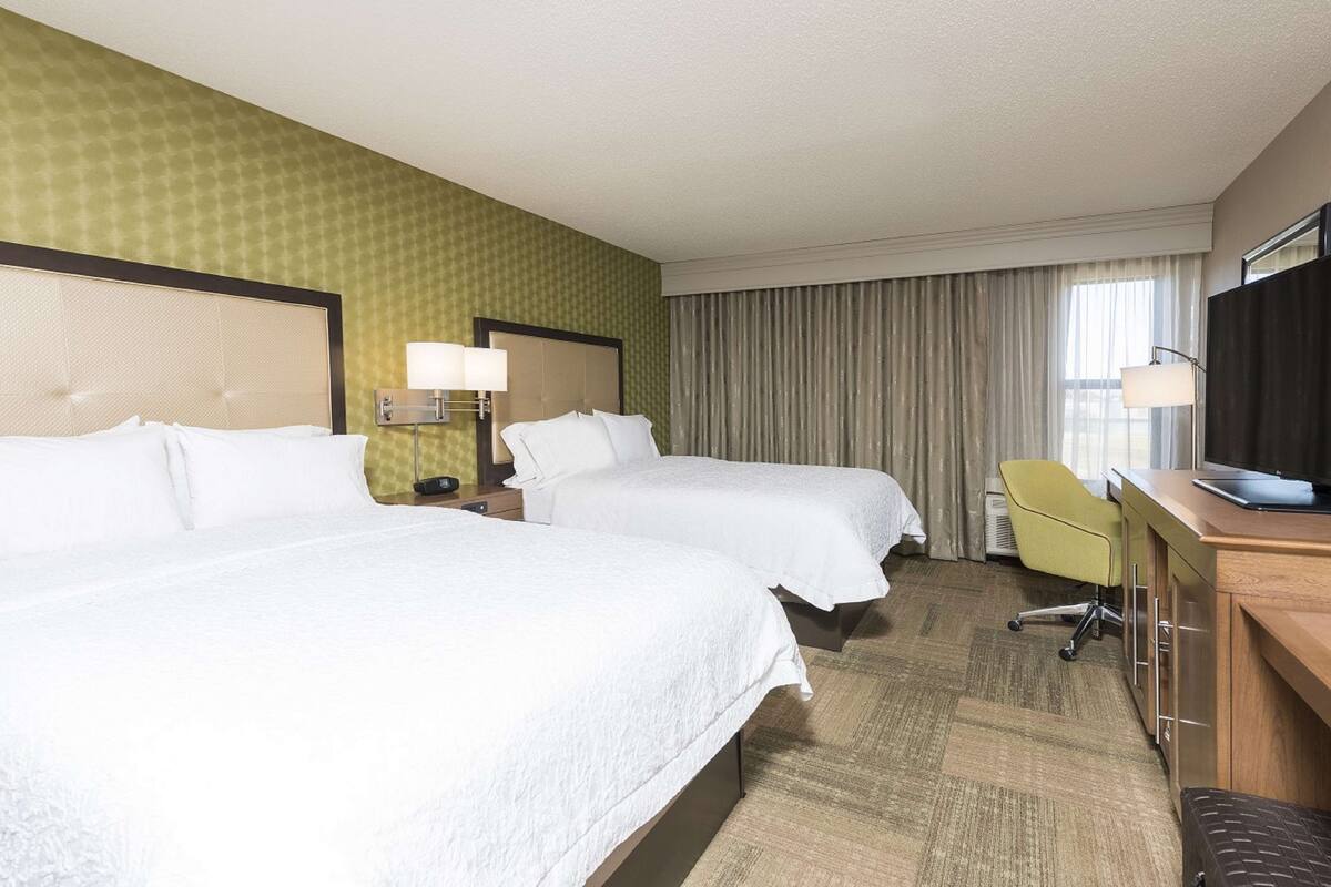 A hotel room with two beds, a desk, a chair, and a television.