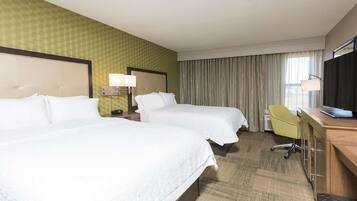A hotel room with two beds, a desk, a chair, and a television.