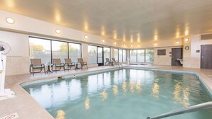 An indoor swimming pool with clear glass walls, several lounge chairs, and a ceiling with recessed lighting.