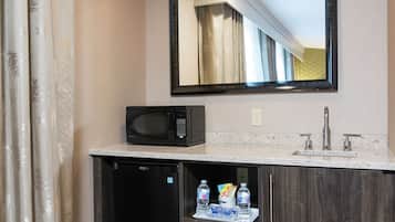 A bathroom with a microwave, sink, and a shelf with bottled water and snacks.