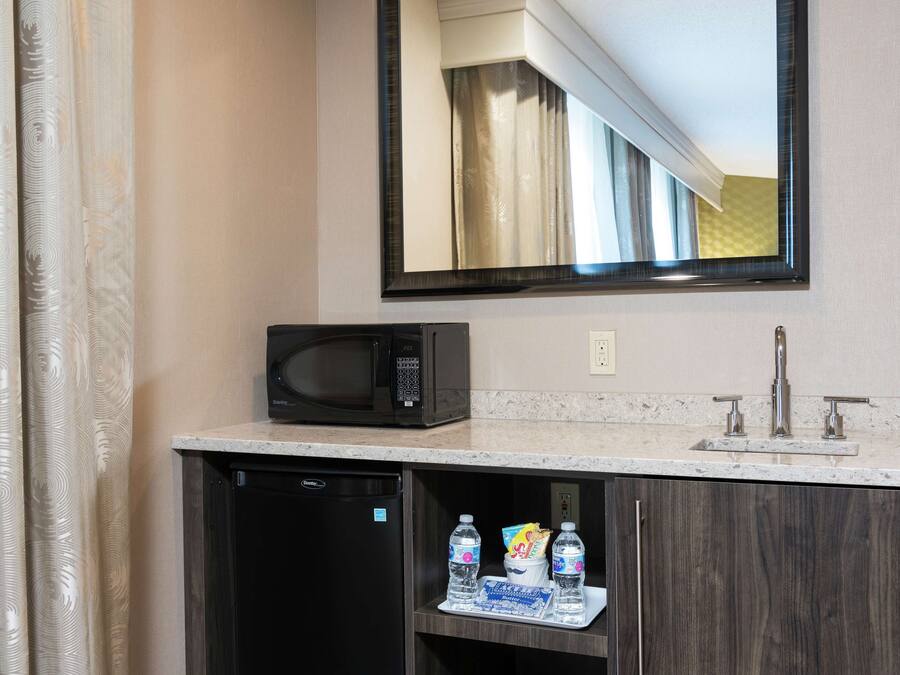 A bathroom with a microwave, sink, and a shelf with bottled water and snacks.