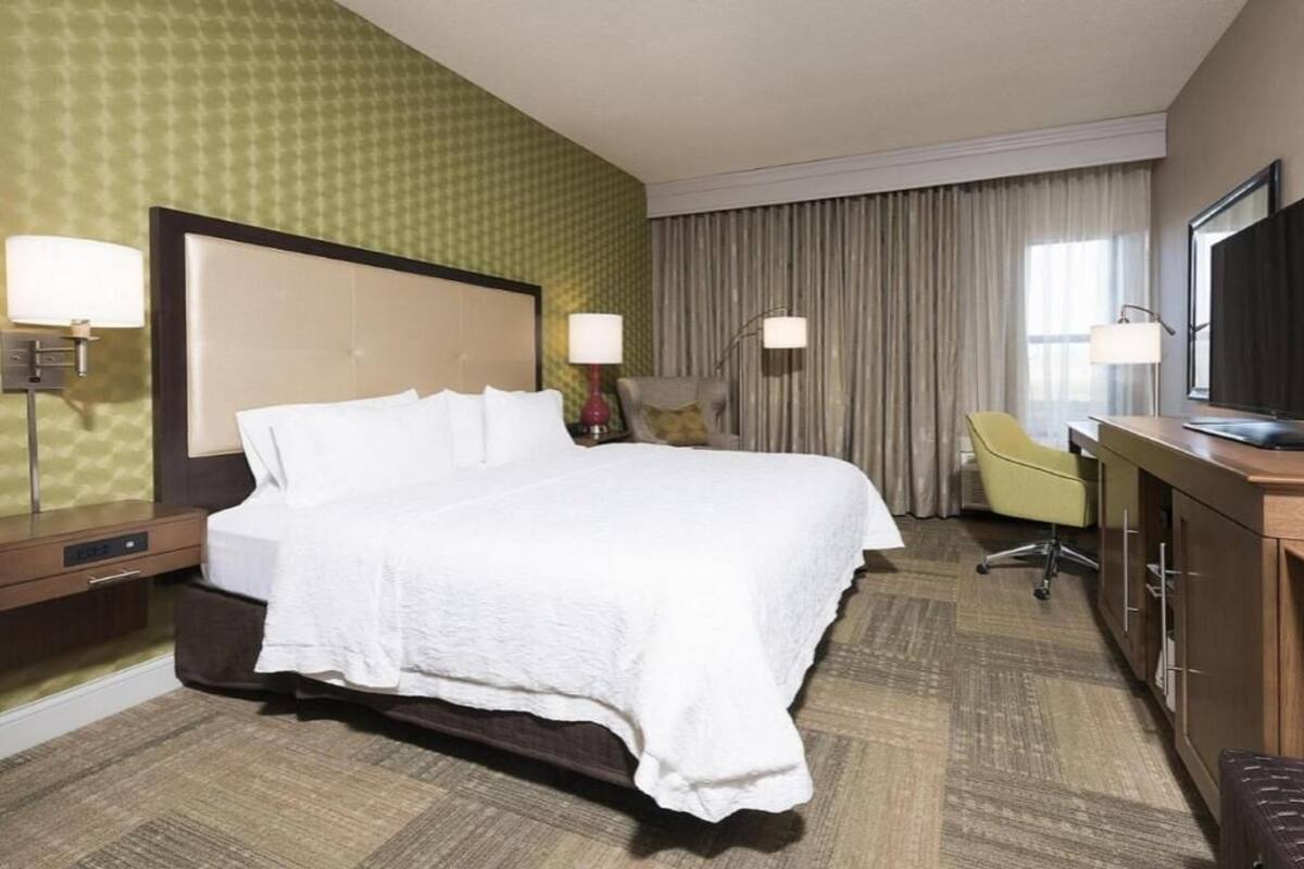 A hotel room with a bed, a desk, a chair, a TV, and a window with curtains.