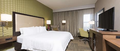 A hotel room with a large bed, a desk with a television, a chair, and a desk lamp.