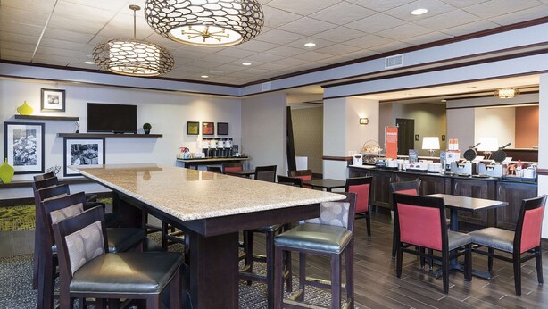 A modern restaurant with a large central table, multiple dining areas, and contemporary lighting fixtures.