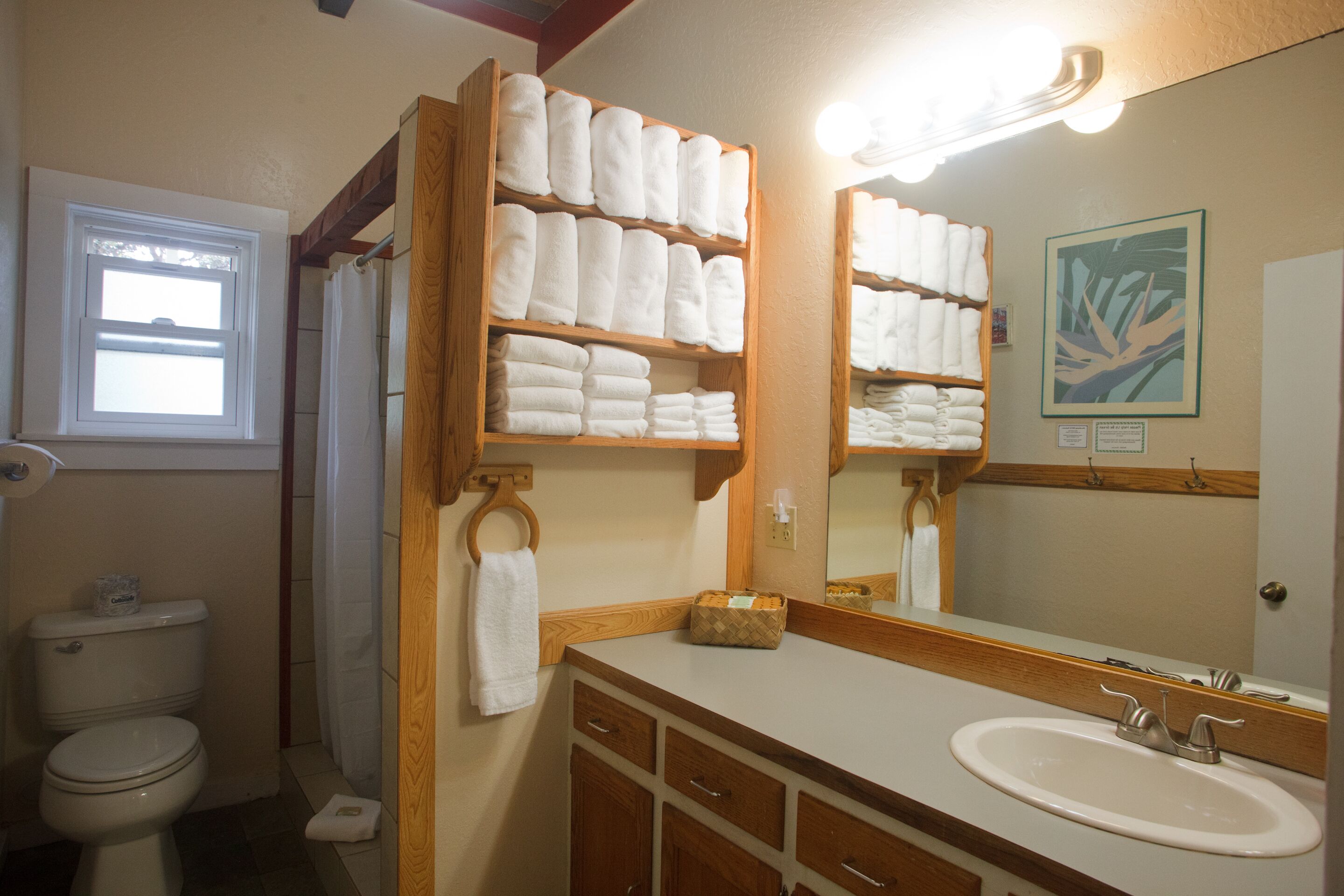 Une salle de bain avec un meuble-lavabo en bois, un évier et un miroir. On y trouve des étagères avec des serviettes pliées et un rideau de douche.