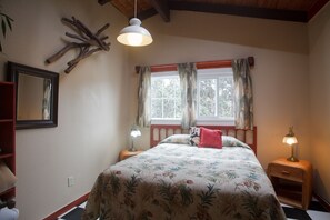 A bedroom with a bed, two bedside lamps, a window with curtains, a wooden headboard, a mirror, and a wall-mounted light fixture.