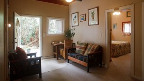 A cozy living room with a wooden bench, a sofa, and a small table with a plant. There are framed pictures on the wall and a door leading to another room. - Volcano Hale (Volcano)