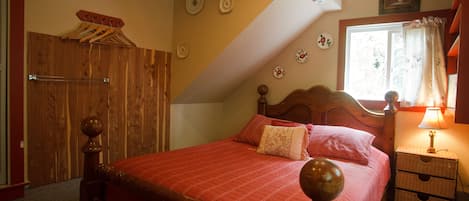 A bedroom with a wooden bed, a nightstand with a lamp, a window with curtains, and a wooden wardrobe.