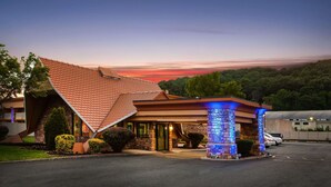 Un hotel con un techo inclinado característico, una entrada bien iluminada y un área de estacionamiento.