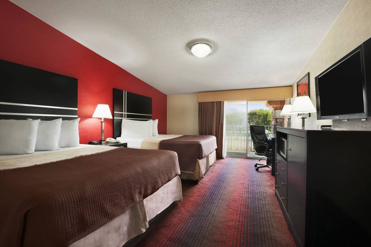 Une chambre d’hôtel avec deux lits, une télévision, un bureau avec un ordinateur et une vue sur l’extérieur.