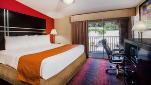 Habitación de hotel con una cama grande, un escritorio con silla, una lámpara y vistas al exterior.