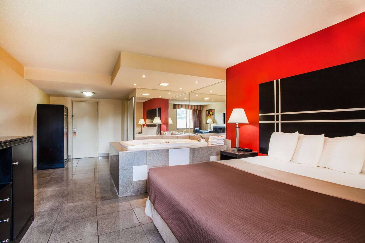 Une chambre d’hôtel moderne avec un grand lit, une salle de bain dotée d’un meuble-lavabo et un mur d’accent de couleur rouge.