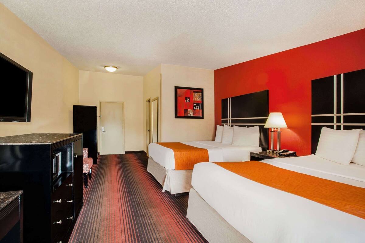 Une chambre d’hôtel avec deux lits, une télévision, un bureau et un mur d’accent rouge.
