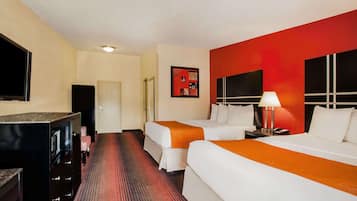 A hotel room with two beds, a TV, a minibar, and a red accent wall.