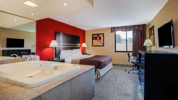 Una habitación de hotel con una bañera grande, una cama, un escritorio y un televisor.