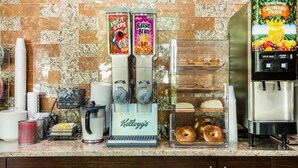 Una kitchenette con cafetera, dispensador de zumo de fruta, máquina de café y refrigerador.
